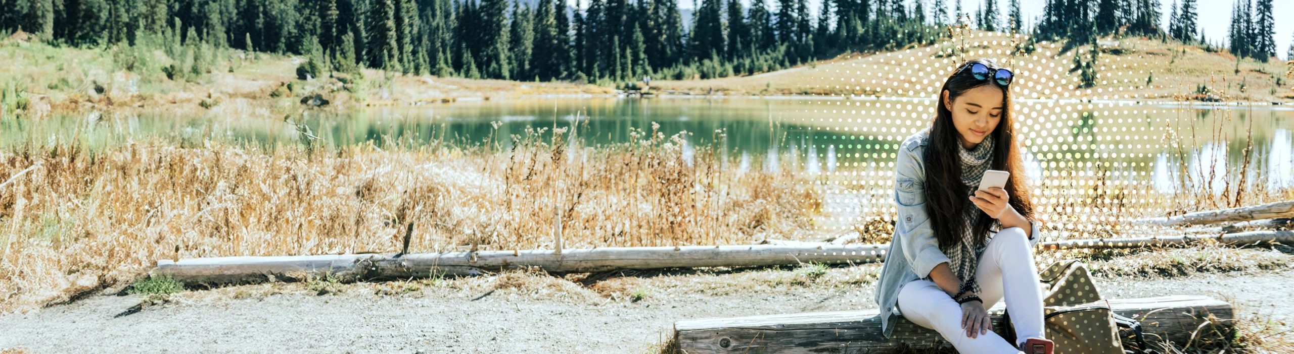 girl sitting by lake looking at her phone