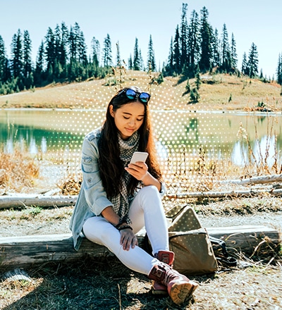girl sitting by lake looking at her phone