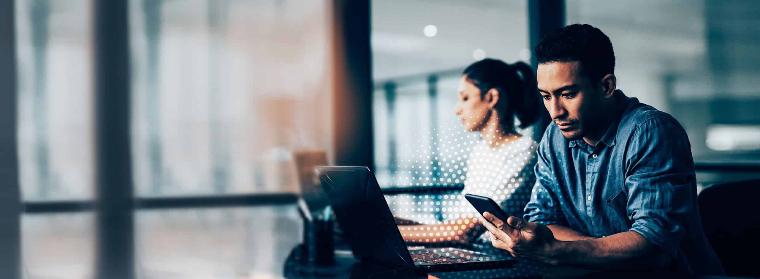 man looking at phone, woman working on laptop