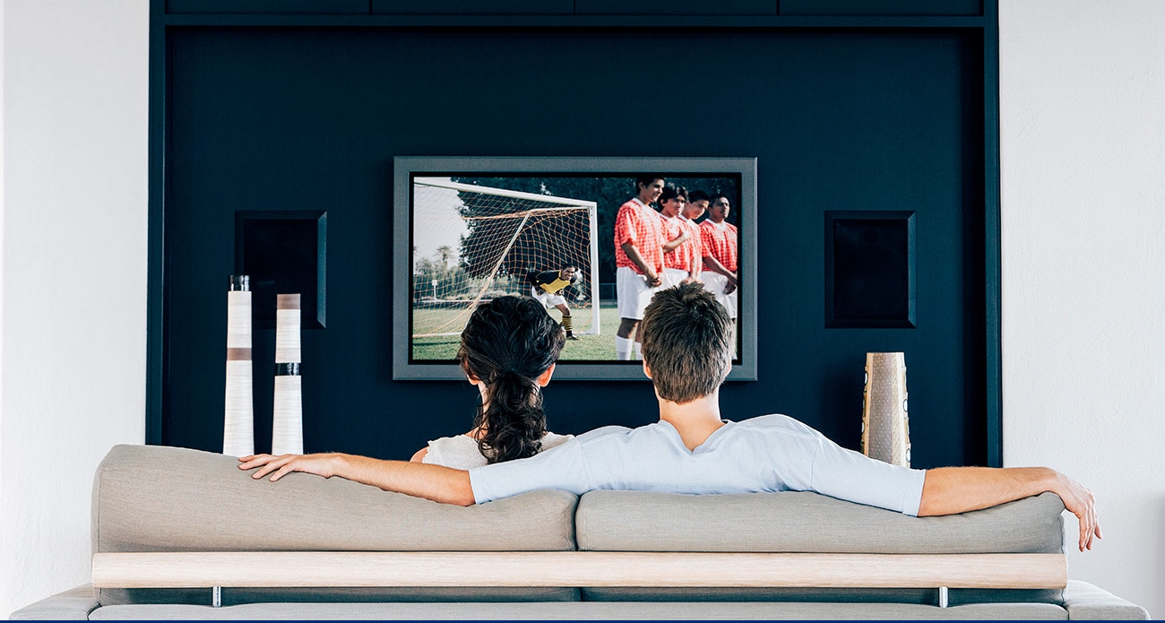 Couple watching a soccer game on their television, emphasizing expanded media connectivity and viewership.
