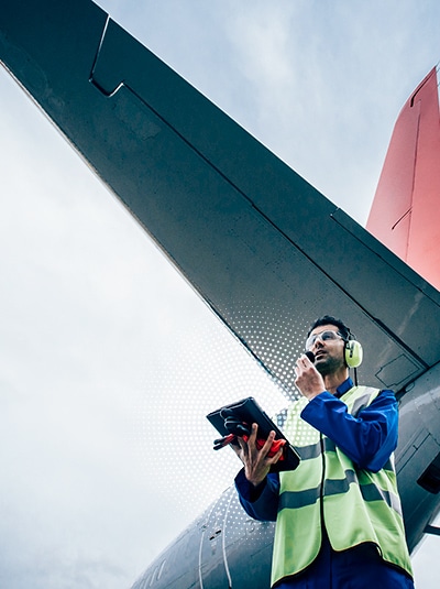 a man wearing a safety vest and headphones under an airplane tail
